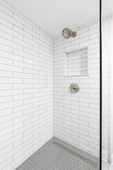 A bathroom shower with white subway tile walls, a built-in niche shelf, bronze shower head, and a...