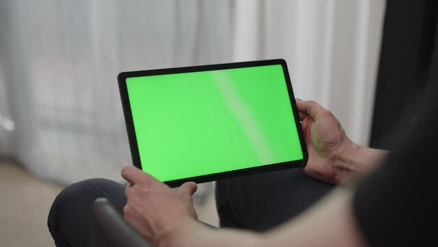 Man sitting indoors on a chair with tablet pc with green screen