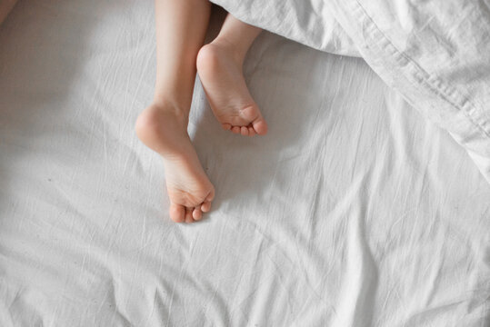 Baby feet under white cotton bed linen. Morning natural light.