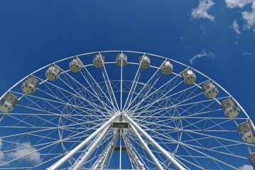 giant ferris wheel detail. white gondolas. steel frame construction. giant spokes in large wheel. leisure and relaxation concept. parks and outdoors. blue sky and white clouds. entertainment and fun
