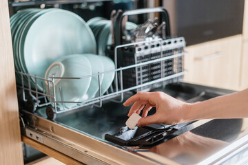Female hand inserting dishwasher tablet into open built-in dishwasher machine