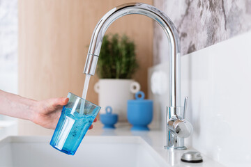 woman filling glass with water from tap at modern apartment
