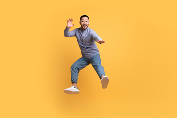 Fototapeta na wymiar Carefree asian man in casual outfit jumping in air over yellow background