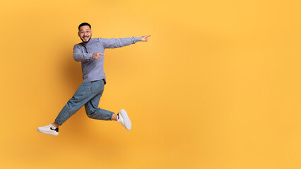 Fototapeta na wymiar Look At This. Cherful asian man pointing aside while jumping in air