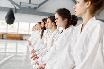 Fototapeta na wymiar Young aikido students wearing kimono sitting on floor in row