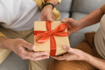 Unrecognizable senior spouses holding wrapped paper gift box with red bow, celebrating valentine day or anniversary