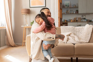 Loving Asian Dad Embracing Little Baby Daughter In Living Room