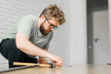 Fototapeta na wymiar Bearded millennial man assemble his bookcase. He uses tools for furniture. Furniture for the interior room or apartments