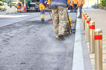 A team of road service workers lays fresh asphalt at a road construction site.