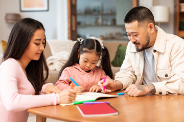 Asian Mom And Dad Teaching Preschool Daughter To Write Indoors