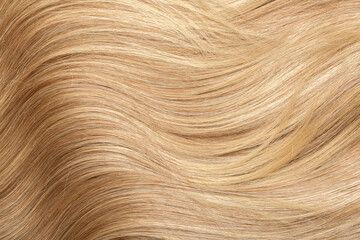 Blond hair close-up as a background. Women's long blonde hair. Beautifully styled wavy shiny curls. Hair coloring. Hairdressing procedures, extension.