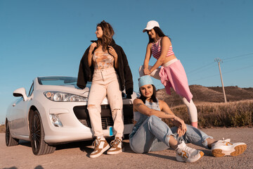 The three friends pose with their white car during a summer trip.