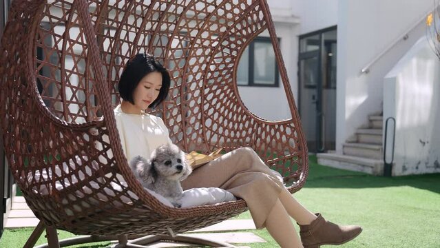Happy young Chinese woman with pet dog on hanging-chair,4K