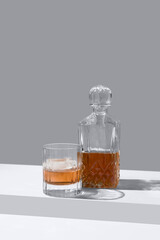 Vaso de whisky con hielo y decantador sobre un fondo gris