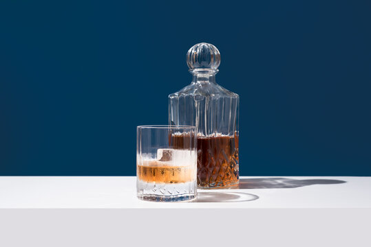 Vaso de whisky con hielo y decantador sobre un fondo azul	