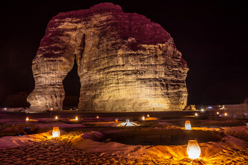 Illuminated outdoor lounge in front of elephant rock erosion monolith standing in the night desert, Al Ula, Saudi Arabia