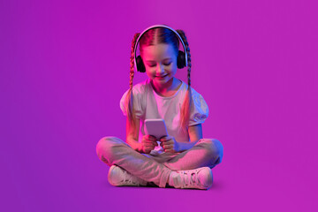 Obraz na płótnie Canvas Preteen kid adorable girl using wireless headphones and smartphone