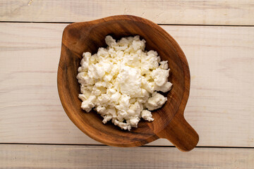Fresh cottage cheese in a wooden cup on a wooden table, macro, top view.