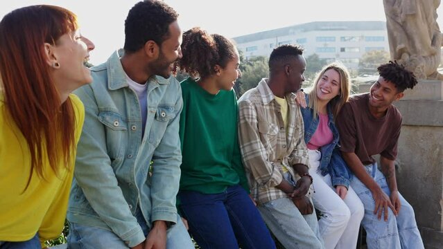 Millennial group of diverse young friends laughing outdoors. Multiethnic hipster people having fun social gathering standing together in city street. Happy lifestyle and youth community concept