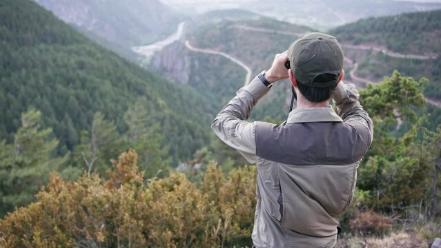 Young man with cap and uniform holds binoculars and looks into the distance, Ranger watching the territory, the protection of the wildlife reserve