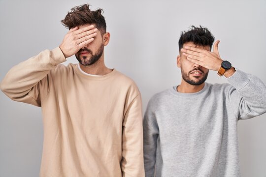 Young Homosexual Couple Standing Over White Background Covering Eyes With Hand, Looking Serious And Sad. Sightless, Hiding And Rejection Concept