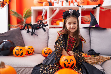 Fototapeta premium Adorable hispanic girl wearing halloween costume holding candy of pumpkin basket at home