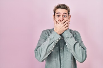 Hispanic man with beard standing over pink background shocked covering mouth with hands for...