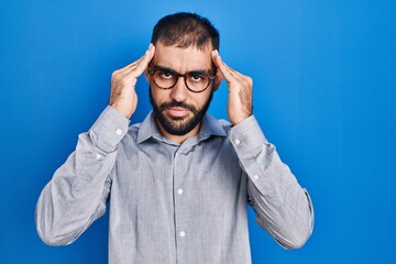 Middle east man with beard standing over blue background with hand on head for pain in head because stress. suffering migraine.