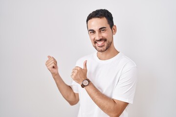 Handsome hispanic man standing over white background pointing to the back behind with hand and thumbs up, smiling confident