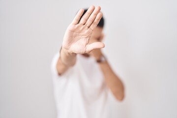 Obraz premium Handsome hispanic man standing over white background covering eyes with hands and doing stop gesture with sad and fear expression. embarrassed and negative concept.