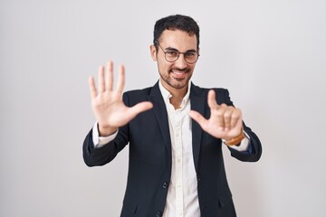 Naklejka premium Handsome business hispanic man standing over white background showing and pointing up with fingers number seven while smiling confident and happy.