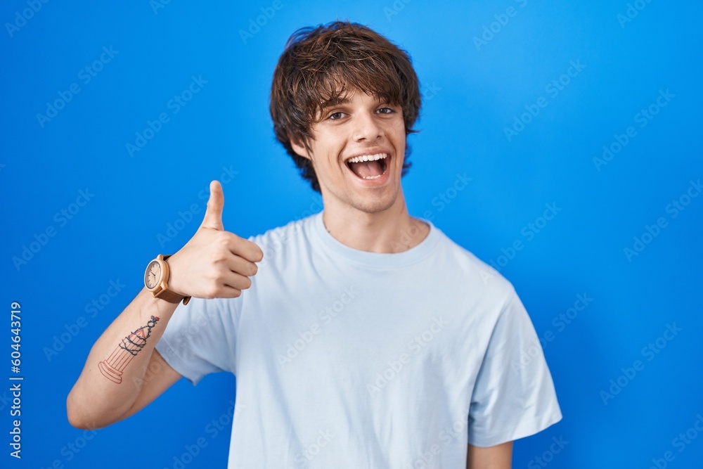 Wall mural hispanic young man standing over blue background doing happy thumbs up gesture with hand. approving 