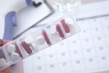 Fototapeta premium Calendar with pills and non-contact thermometer on light background.