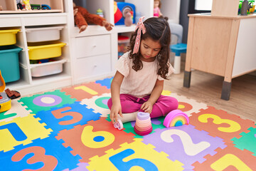 Adorable hispanic girl playing with heart blocks sitting on floor at kindergarten