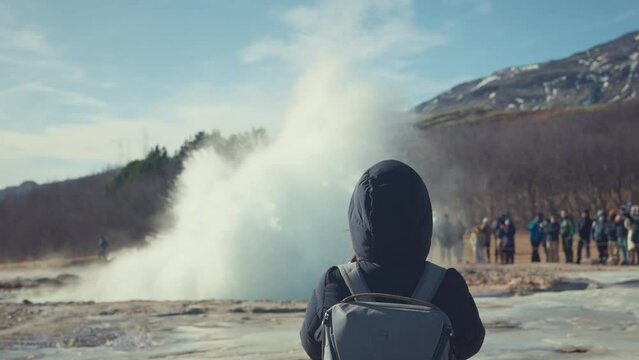 Rear view - Tourist woman stops to take a looking at Erupting geyser Strokkur, Iceland. Strokkur is part of geothermal area, Cinematic