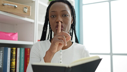 African american woman teaching with book asking for silence at university classroom
