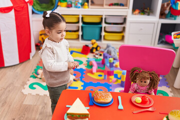Adorable hispanic girl playing with food and doll at kindergarten