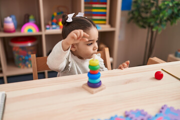 Adorable hispanic girl playing with hoops toys sitting on table at kindergarten