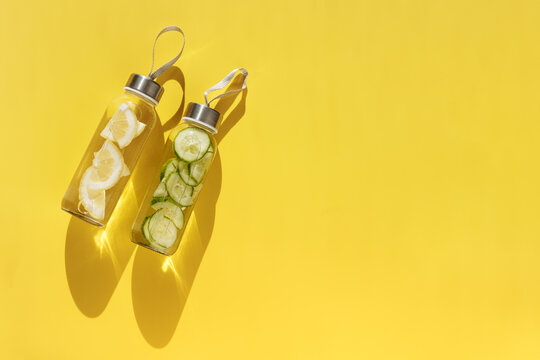 Water drink detox with slices of lemon and cucumber, shadow at sunlight on yellow background. Wellness, diet, eating healthy concept. Stylish glass reusable water bottle, still life top view