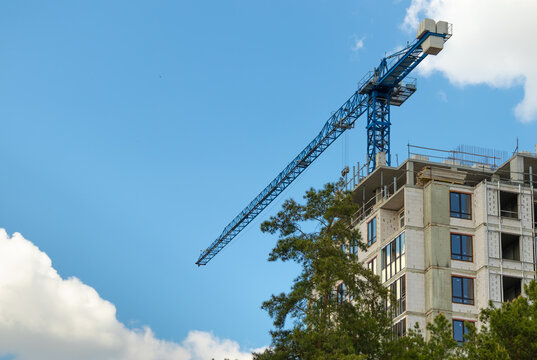 Construction crane and building a house against a blue sky with clouds