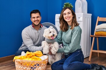 Man and woman washing clothes with dog at laundry room