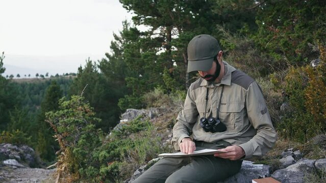 Young man with cap and uniform holds binoculars and a map and looks into the distance, Ranger watching the territory, the protection of the wildlife reserve