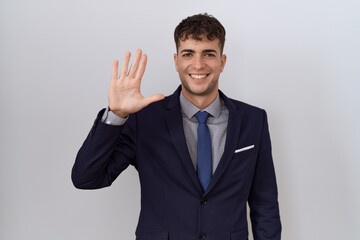 Young hispanic business man wearing suit and tie showing and pointing up with fingers number five while smiling confident and happy.