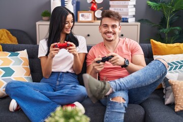 Man and woman couple playing video game sitting on sofa at home