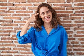 Beautiful brunette woman standing over bricks wall smiling pointing to head with one finger, great idea or thought, good memory