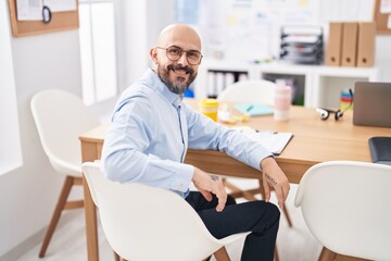 Young bald man business worker smiling confident sitting on table at office