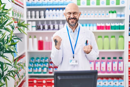 Hispanic man with tattoos working at pharmacy drugstore celebrating surprised and amazed for success with arms raised and eyes closed