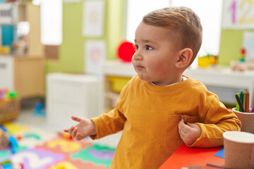 Adorable blond toddler standing with relaxed expression at kindergarten