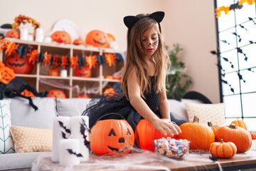 Adorable hispanic girl wearing halloween costume holding candies of bowl at home