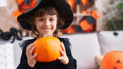 Adorable hispanic girl having halloween party holding pumpkin at home